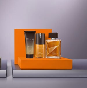 Três produtos da linha Natura Essencial (um shower gel em bisnaga, um desodorante corporal spray e um perfume em frasco de vidro) organizados sobre uma plataforma laranja. 