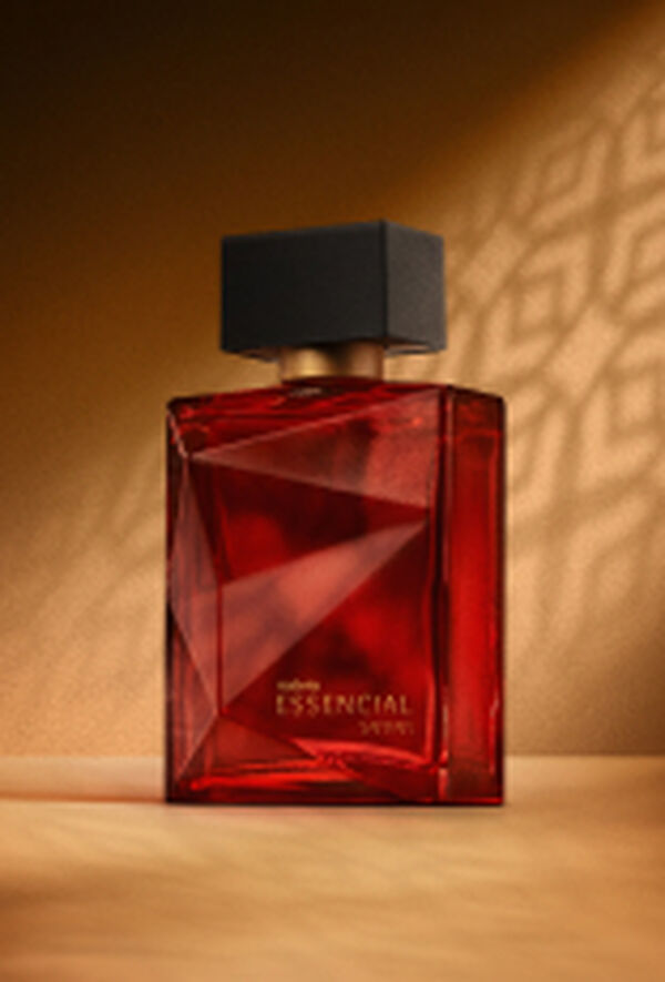 Deo Parfum Essencial Safran Masculino em frasco facetado vermelho com tampa preta. Está em fundo cor areia com sombra geométrica projetada.