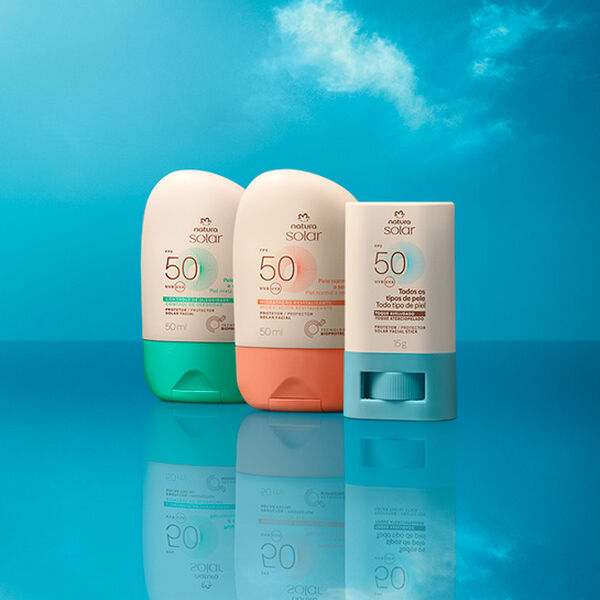 Embalagens Natura Solar Faciais FPS 50 lado a lado: creme com verde para pele mista, creme com laranja para pele normal e stick creme com azul para todos os tipos de pele, sobre fundo de céu azul.