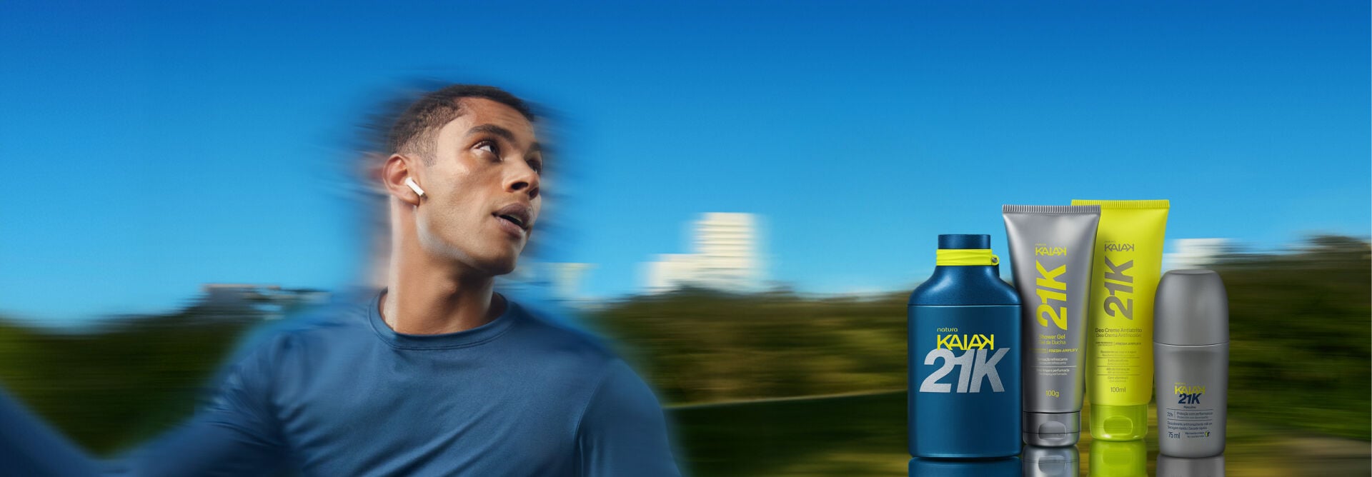 Banner ao ar livre com homem de camiseta azul correndo em velocidade. À direita, perfume azul Kaiak 21K, shower gel cinza, deo creme atrito amarelo e desodorante roll-on cinza.