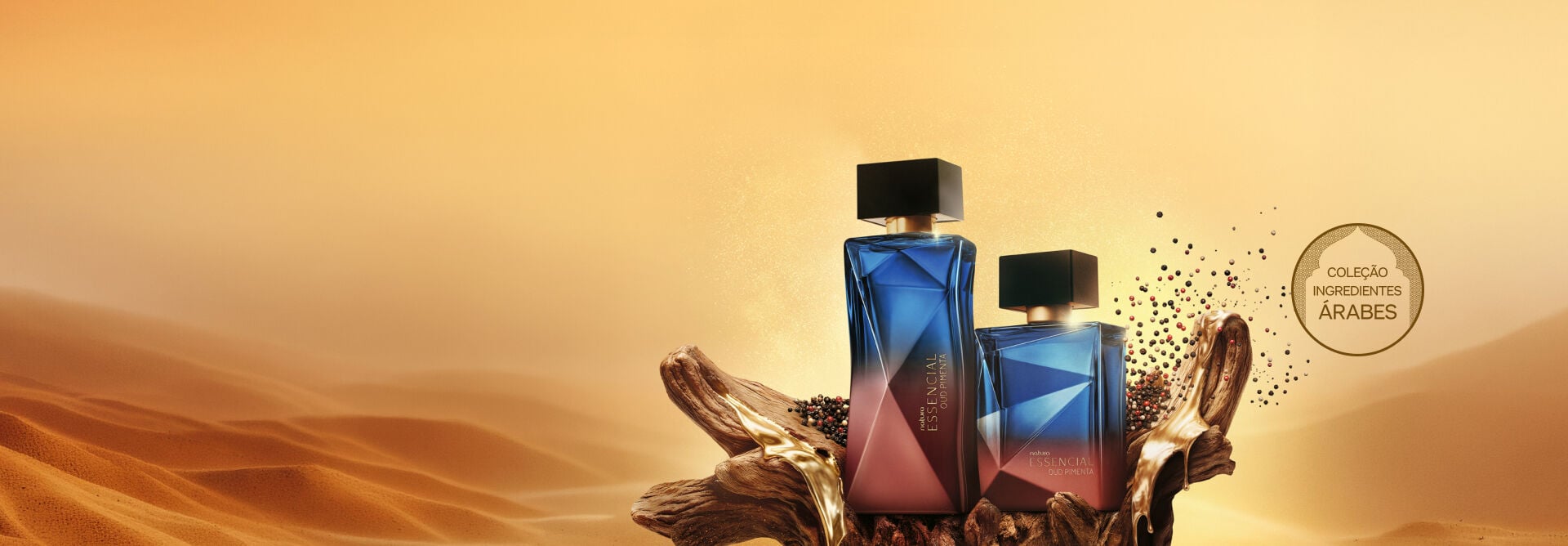 Frascos de Natura Essencial Oud Pimenta feminino e masculino sobre tronco com resina dourada em cenário desértico. Ao lado, pimentas dispersas no ar e selo "Coleção Ingredientes Árabes". 