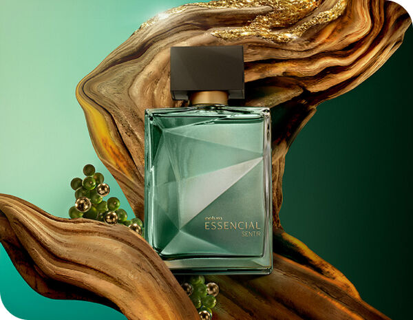 Frasco do perfume Essencial Sentir Masculino, em vidro verde com tampa marrom fosca, posicionado ao centro, cercado por galhos e sementes verdes, sobre um fundo em tons de verde degradê.