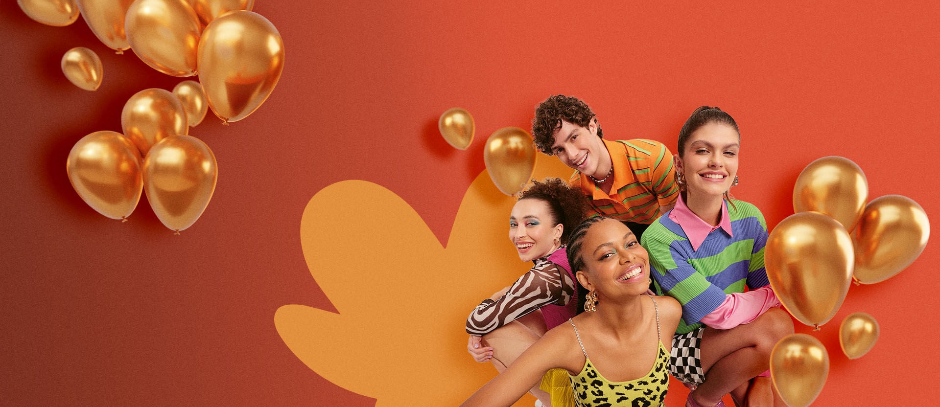 Quatro jovens sorridentes — três mulheres e um homem — posam à esquerda de um fundo laranja vibrante. Eles vestem roupas coloridas com estampas diversas, como animal print e listras. Ao redor do grupo e flutuando à esquerda, há diversos balões dourados metálicos de diferentes tamanhos.