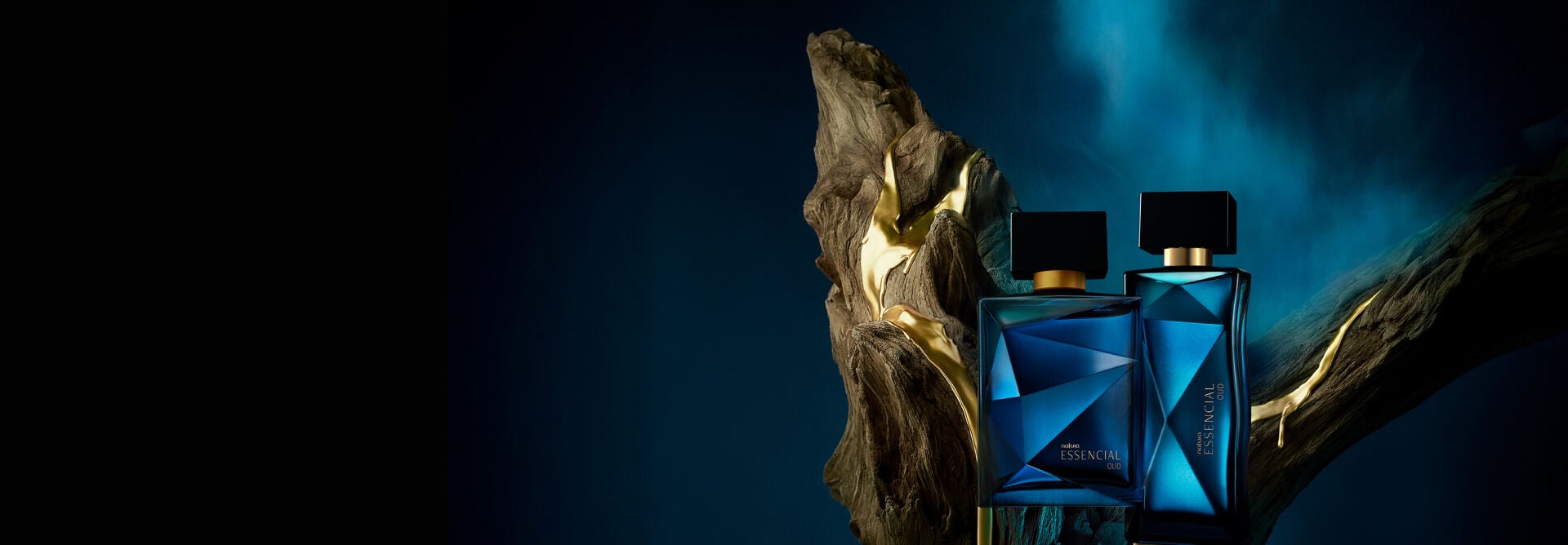 Frascos azuis de Natura Essencial Oud, masculino e feminino, sobre tronco de madeira, em fundo azul-escuro.