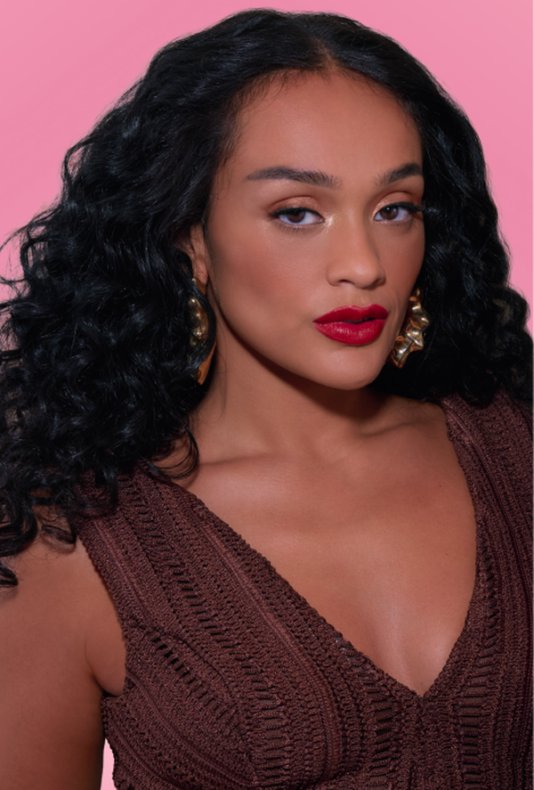 Três mulheres: uma com top branco, cabelo castanho curto e pele branca, uma com blusa marrom, pele negra e cabelo curto, e uma com top preto, cabelo longo liso e pele branca. Fundo degradê rosa-claro.