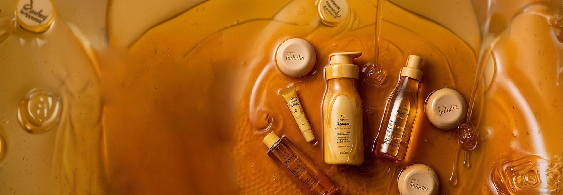 Produtos Natura Tododia Néctar de Mel imersos em mel líquido amarelo âmbar. A linha inclui hidratante, body splash, óleo corporal, sabonetes em barra e gloss labial.