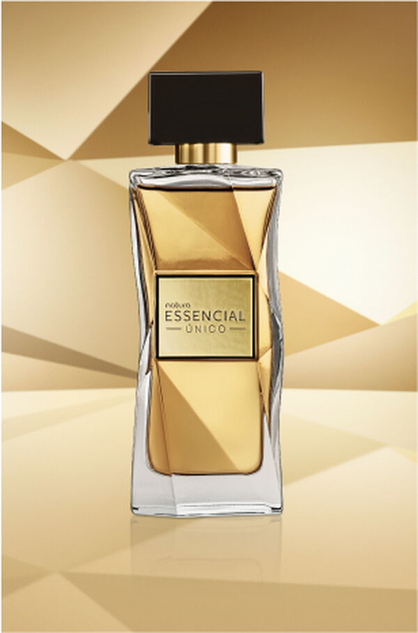 Frasco de Essencial Oud Feminino, em tom de azul-escuro e tampa preta, aparece em destaque no centro da tela sobre fundo multifacetado dourado, fazendo alusão ao design do frasco de Essencial.