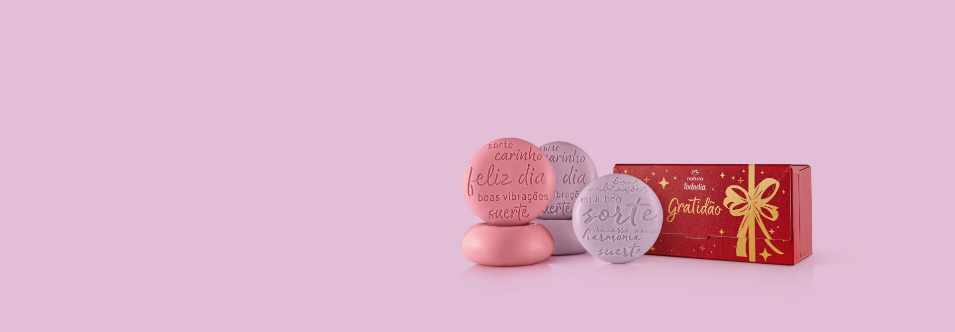 presente tododia sabonetescom sabonetes vermelhos e lilás, com uma caixa de embalagem de presente. Ambos em um fundo rosa claro.