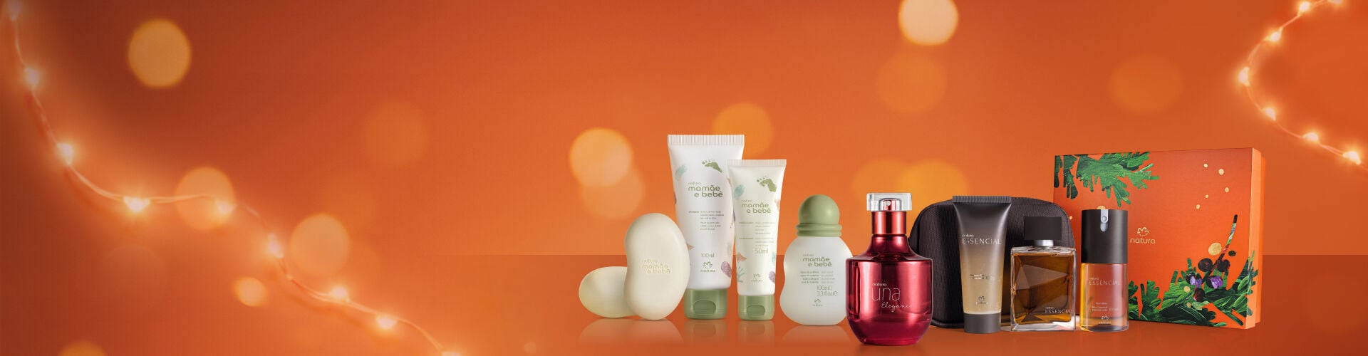 Seleção de presentes Natura reunindo produtos Mamãe e Bebê, Una e Essencial em fundo alaranjado com luzes desfocadas, celebrando a diversidade de rituais de cuidado para toda a família.