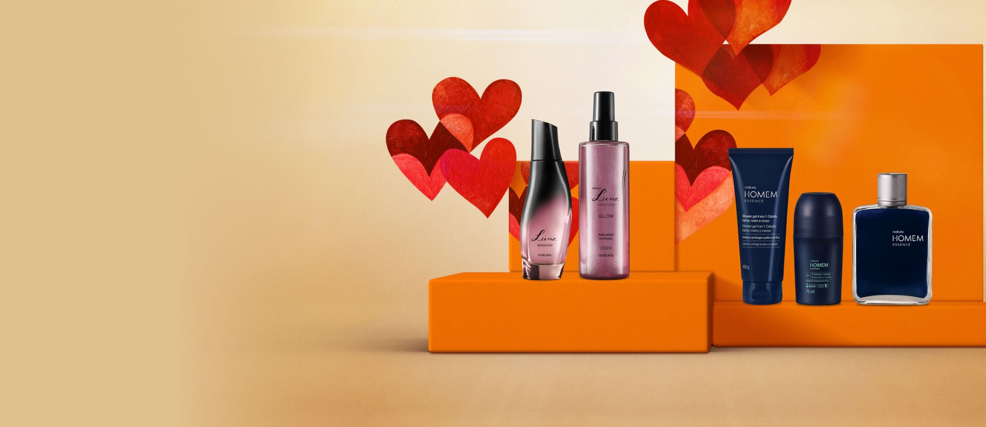 presentes de dia dos namorados Natura posicionados lado a lado em uma bancada laranja. À esquerda, dois frascos da linha feminina Luna Absoluta; à direita, três produtos da linha masculina Natura Homem Essence em tons de azul-escuro.