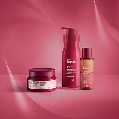 Produtos de Tododia Cereja e Avelã: 1 pote de Creme Amanteigado Corporal Perfumado, 1 Creme Desodorante Nutritivo para o Corpo e 1 Óleo Bifásico Corporal. Embalagens vermelhas em fundo vermelho.