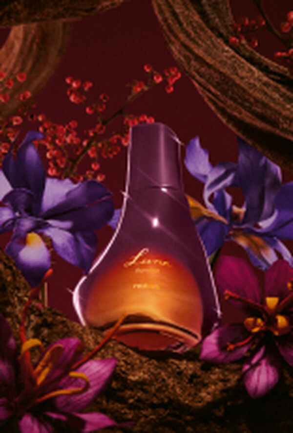 Frasco de Deo Parfum Luna Ilumina Feminino em tons de rosa e laranja sobre fundo vinho, flores violetas, troncos e texturas de madeira.