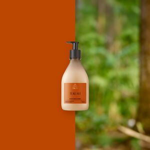 Frasco bege com pump preto do Creme Desodorante Hidratante para o Corpo Natura Ekos Tukumã ao centro. Fundo dividido entre laranja terroso e floresta desfocada em tons de verde.