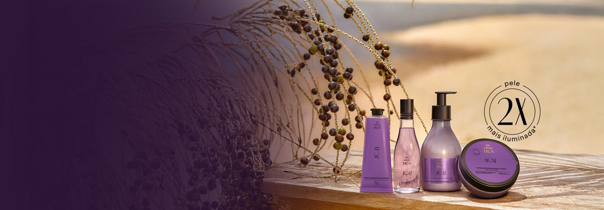 Linha Ekos Açaí, incluindo 1 polpa para mãos, 1 frescor, 1 creme iluminador para o corpo e 1 esfoliante em pó, repousa sobre superfície de madeira à beira-mar com ramos e frutos de açaizeiro. Selo aplicado: pele 2X mais iluminada.