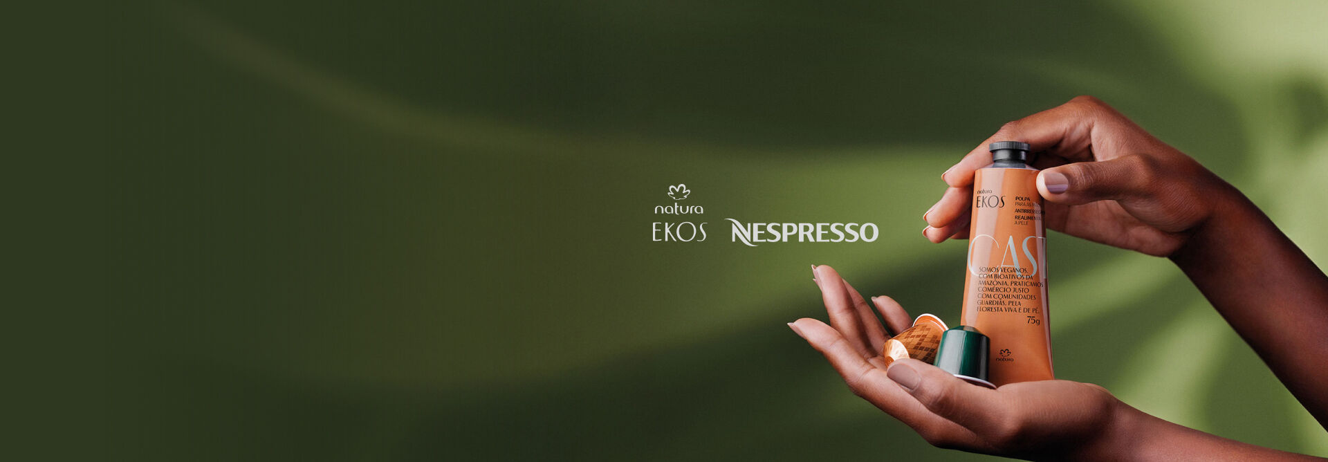 Fundo verde com duas mãos segurando uma embalagem do creme de mãos Natura Ekos Castanha e cápsulas de café Nespresso.  Na parte superior logo Natura Ekos e Nespresso.