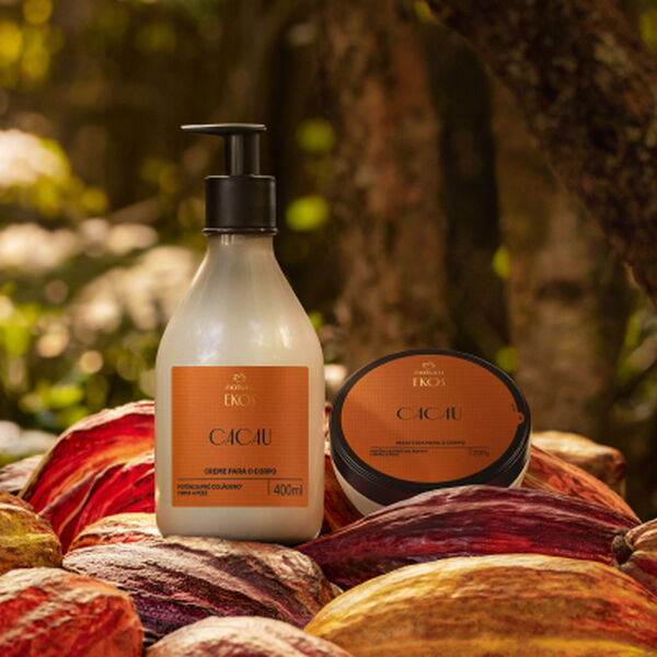 Polpa Hidratante para o Corpo e Manteiga Hidratante para o Corpo Ekos Cacau, com frascos transparentes e conteúdos bege-claros, tampas pretas e rótulos laranjas, repousam sobre frutos de cacau em meio à floresta. 
