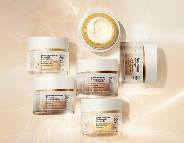 Foto de 6 frascos de Creme Antissinais Chronos Derma, incluindo produtos para diferentes idades. Os potes estão sobre fundo claro com raios de luz. 