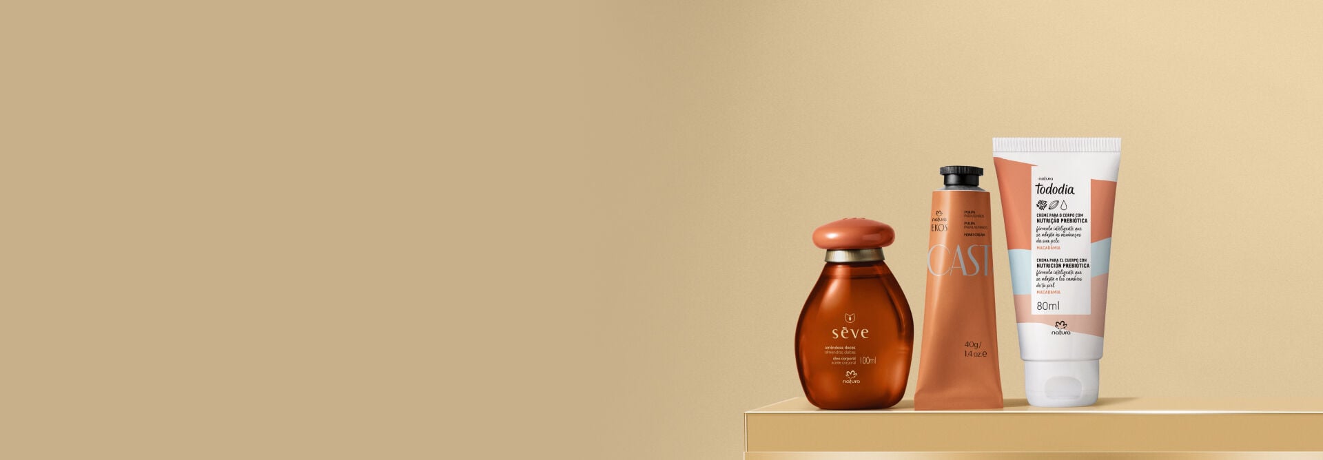 Presente Natura Queridinhos, com 1 Óleo Corporal Sève Amêndoas Doces, 1 Polpa para as Mãos Ekos Castanha e 1 Creme Nutritivo para o Corpo Tododia Macadâmia sobre caixas de presentes em fundo bege.  