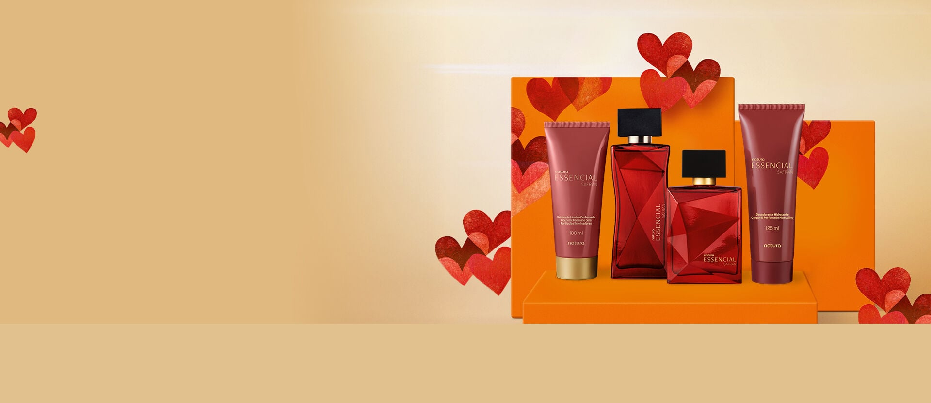 presentes de dia dos namorados Natura Essencial Safran dispostos em uma bancada laranja com decorações de corações vermelhos. Inclui dois frascos de perfume de vidro vermelho e duas bisnagas de creme marrons.