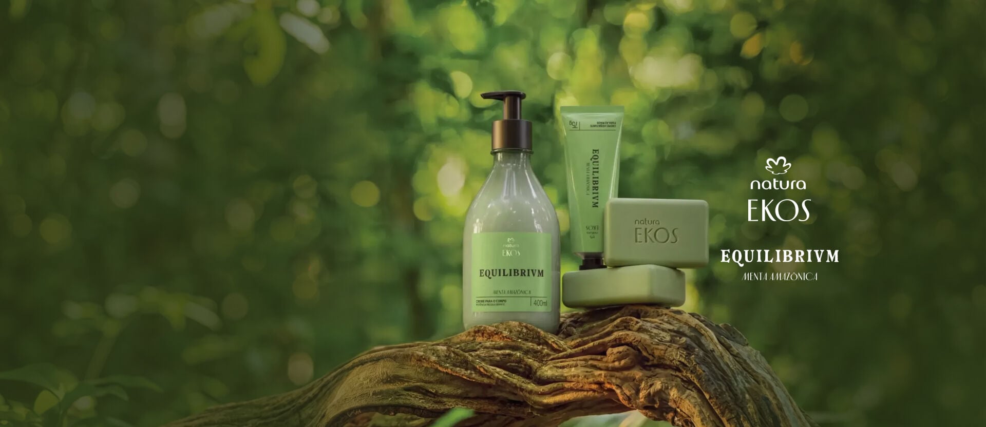 Em destaque sobre tronco, frasco de creme corporal, bisnaga e sabonetes Natura Ekos. Logo Natura Ekos Equilibrivn Menta Amazônica.