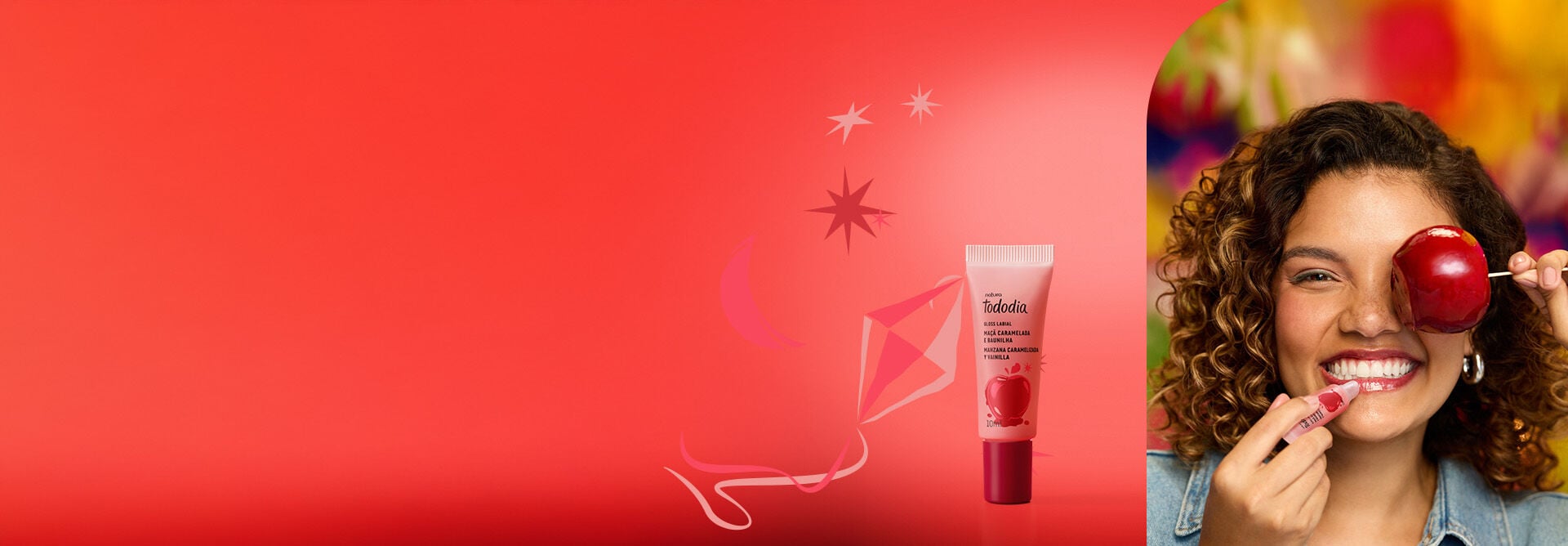 Bisnaga vermelha do Gloss Labial Tododia Maçã Caramelada e Baunilha. A embalagem com tampa vermelha e ilustração de maçã está em fundo vermelho com estrelas e balão de São João.