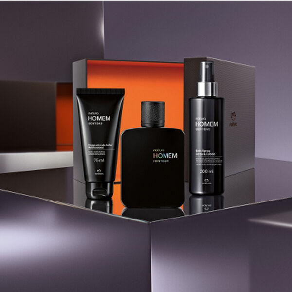 Kit Natura Homem Identidad posicionado sobre uma superfície espelhada à frente de uma caixa aberta. Inclui um creme pré e pós-barba, a colônia em frasco preto fosco e um body spray.