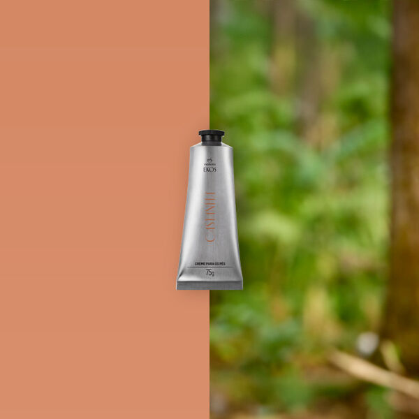 Bisnaga prateada de Creme para os pés  Ekos Castanha 75 g está apoiada sobre um tronco de árvore, cercada por folhas verdes e vegetação densa de floresta ao fundo.