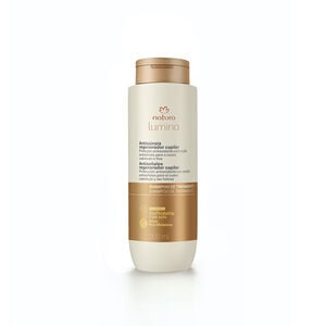 Embalagem creme com tampa e rótulo dourados de Shampoo de Tratamento Antissinais Natura Lumina. Fundo em verde com listras verticais.