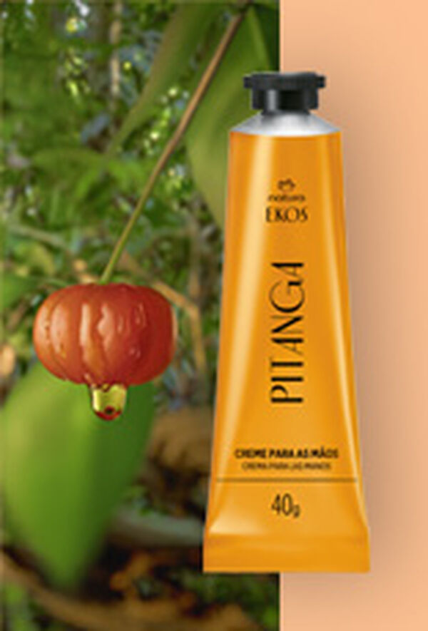 Bisnaga amarela do Creme Hidratante para as Mãos Ekos Pitanga à direita, ao lado de uma pitanga vermelha com gota de extrato, sobre fundo de folhas verdes e laranja suave.