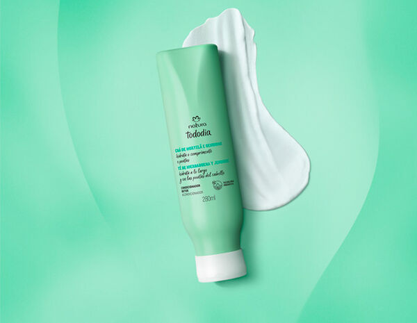 Frasco verde-claro com tampa branca do Condicionador Detox Tododia Chá de Hortelã e Gengibre. Está sobre um rastro de creme branco em fundo degradê verde.