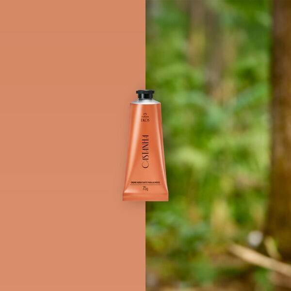 Bisnaga cobre do Creme Hidratante para Mãos Ekos Castanha 75 g ao centro, com castanhas abertas ao lado direito em fundo bege e folhas verdes desfocadas à esquerda.