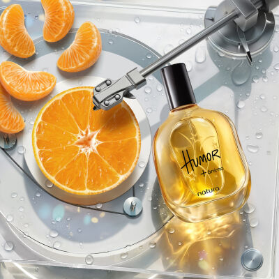 Desodorante Colônia Humor + Ânimo em frasco amarelo com tampa preta. Está em fundo branco ao lado de um toca-discos transparente molhado, com uma rodela de laranja no centro e gomos espalhados.