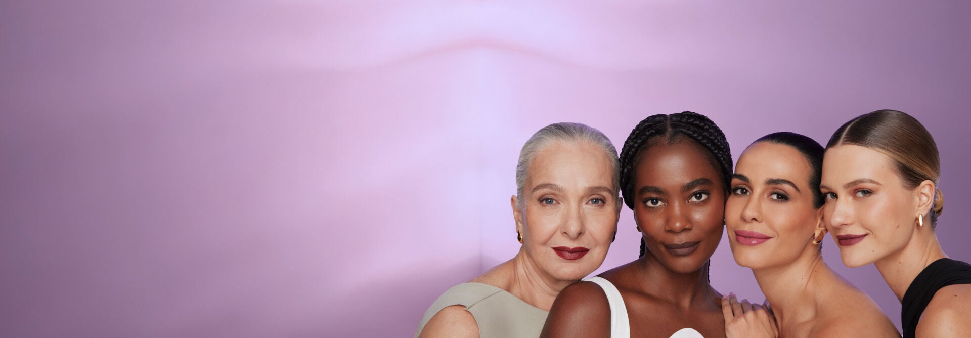 Foto de 4 modelos de diferentes idades. Todas elas estão com cabelo preso, leve sorriso no rosto, usando sombra, blush nas bochechas e batom. Fundo da imagem em degradê lilás.
