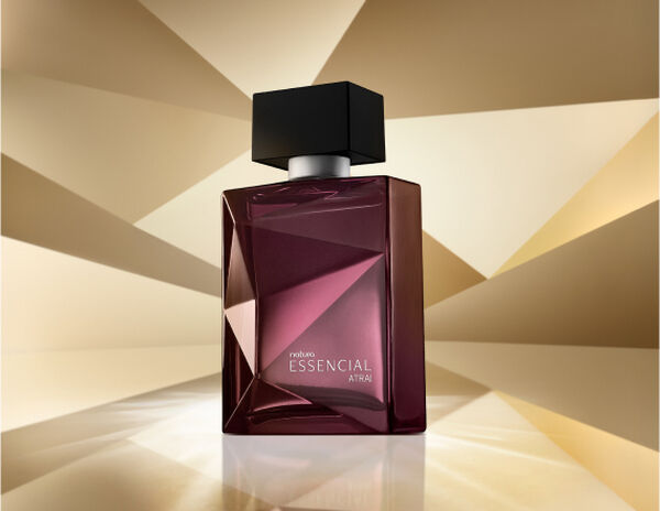 Frasco de Essencial Atrai Masculino, em tons de roxo e violeta com tampa preta, aparece em destaque em fundo dourado multifacetado, fazendo alusão ao design dos frascos de Essencial.