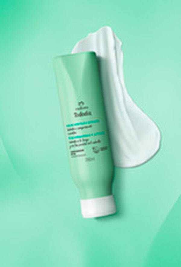 Frasco verde-claro com tampa branca do Condicionador Detox Tododia Chá de Hortelã e Gengibre. Está sobre um rastro de creme branco em fundo degradê verde.