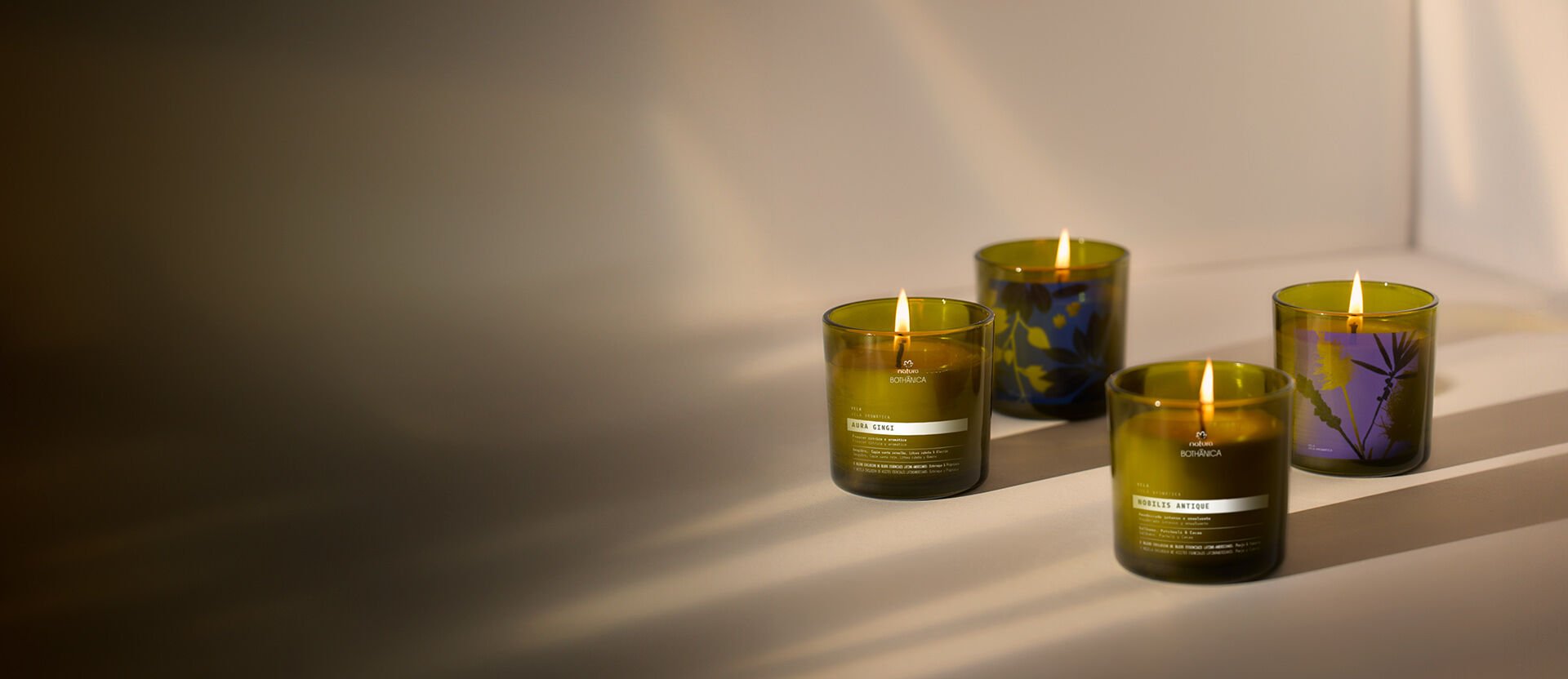 Cuatro velas perfumadas de Natura Bothanica en tonos verdes y morados, alineadas sobre una superficie clara con sombras suaves.