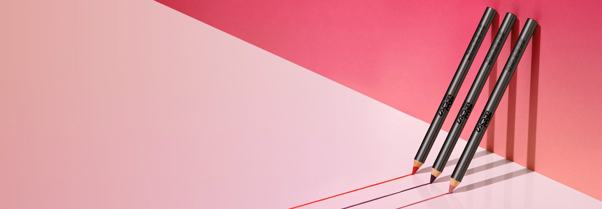 Imagen con fondo rosa claro y, en el lado derecho, tres lápices labiales Natura Una apoyados en la pared.