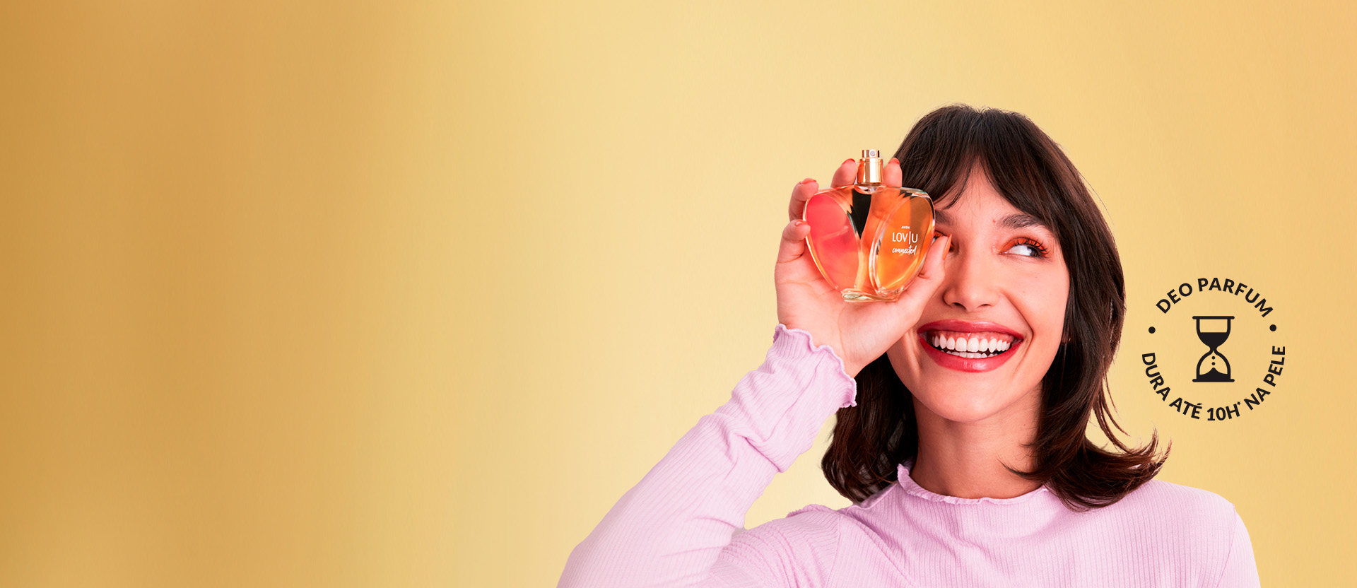 Modelo segurando a fragrância de Avon, Lov|u Connected, com um fundo neutro Amarelo. O frasco lembra um coração. Texto: "Lov|u, apaixone-se pelas fragrâncias!"