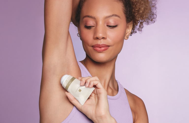 Mulher veste regata roxa e está com os braços levantados passando um antiperspirante diretamente nas axilas.