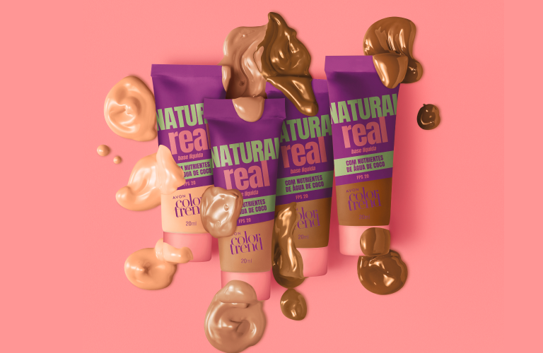 Vista superior de tubos de base com protetor solar da linha "Natural Real" da Avon, dispostos sobre um fundo rosa, cercados por amostras e gotas de base em vários tons da pele, do claro ao escuro.
