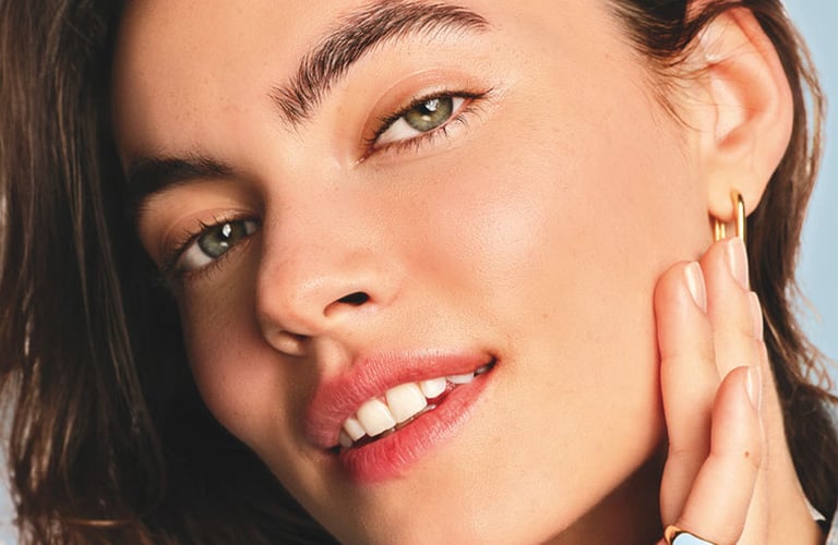 Mulher sorridente de cabelos castanhos, mostrando a pele do rosto sem marcas, com viço e saudável.