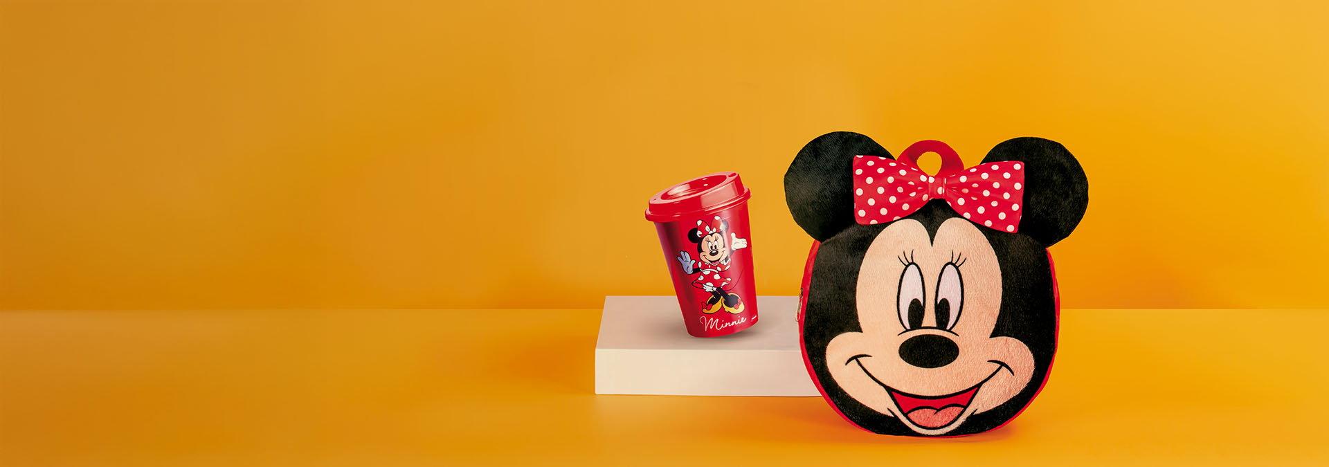 Banner com fundo laranja, aparecem uma caneca vermelha da Minnie e uma almofada em formato da Minnie com laço de bolinhas. Texto: "Kits Casa & Estilo: combinações perfeitas para decorar sua casa!"