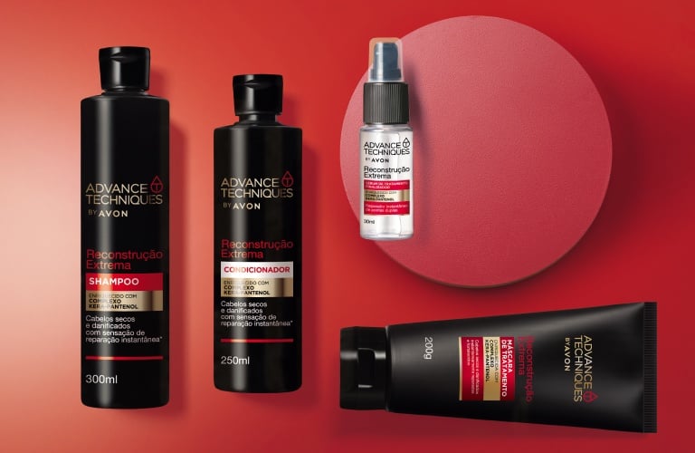 Linha de reconstrução capilar da marca Advance Techniques da Avon com produtos de shampoo, condicionador, sérum e máscara reconstrutora, todos dispostos em um fundo vermelho vivo.