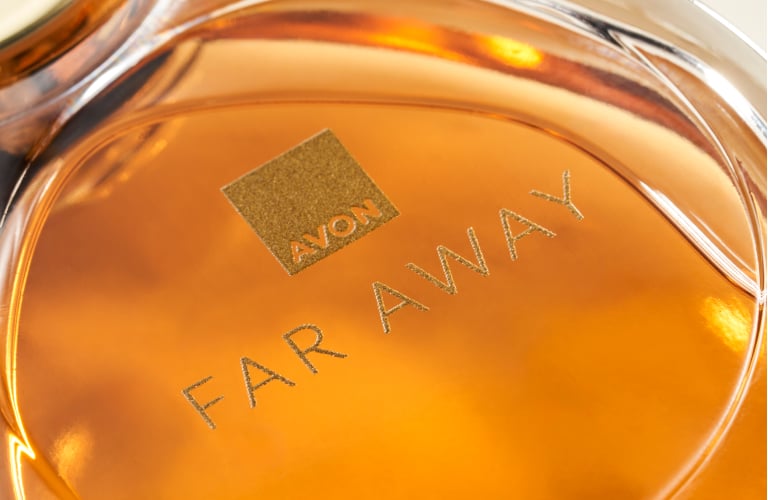 Frasco de vidro de perfume com líquido em um tom âmbar intenso, com o nome "Far Away" gravado no centro.