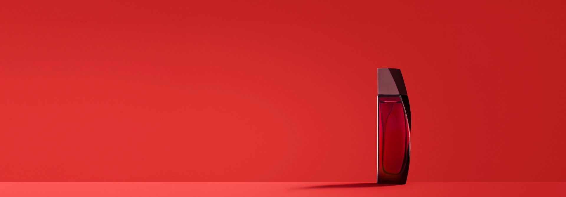 À direita, frasco vermelho com tampa marrom de fragrância Power Stay em fundo vermelho.