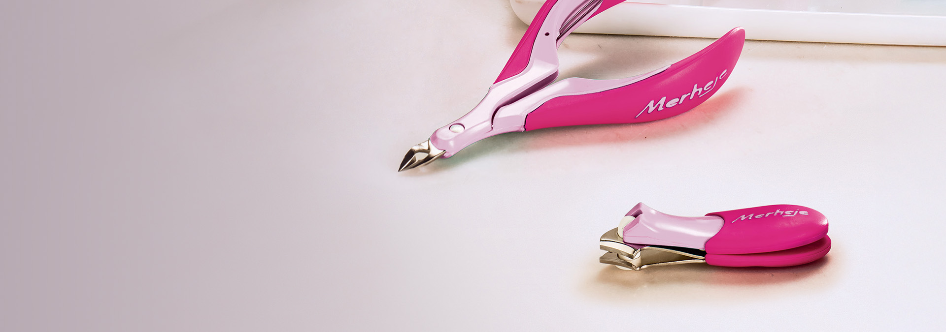 Banner com fundo neutro, apresentando um cortador de unhas e um alicate rosa da marca Merhje. O texto destaca "Acessórios para as unhas" e sugere produtos essenciais para unhas impecáveis e estilosas.
