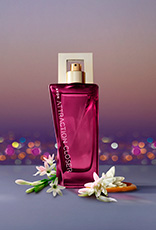 Fragrância Avon Attraction Closer para Ela em bancada cinza com ingredientes, como cítricos e flores, em fundo de entardecer de uma cidade iluminada.