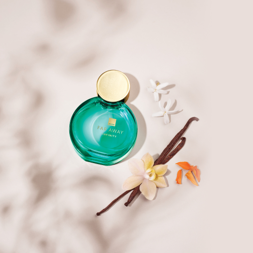 Frasco verde-água redondo com tampa dourada de Far Away Infinity sobre fundo claro com flores brancas, orquídea amarela, favas de baunilha e pétalas laranja.