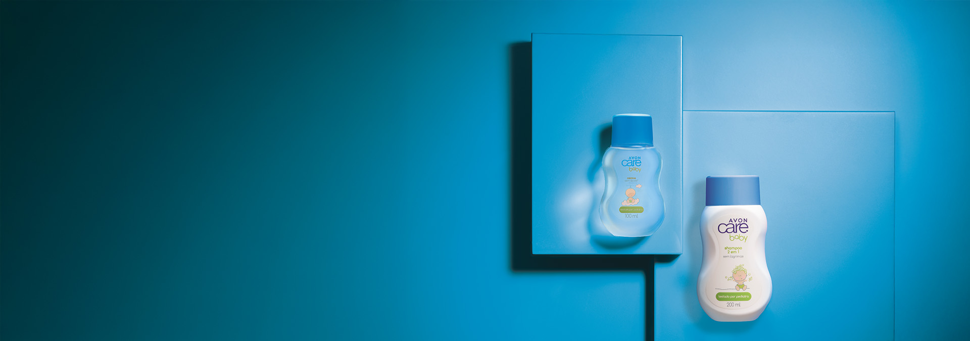 Banner com fundo azul em diferentes tons. Frascos Avon Care Baby: um transparente e outro branco com tampa azul, posicionados sobre duas caixas. Texto: "Amor e proteção para a pele dos bebês."