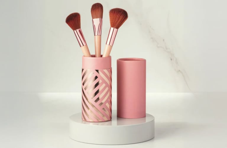 Pote rosa e dourado contendo um pincel de maquiagem de cerdas cheias e fofas, um pincel língua de gato e um pincel chanfrado para blush e contorno.